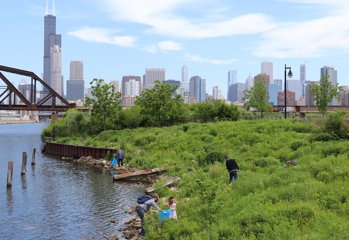 People relax alongside a river with the Chicago skyline in the background.